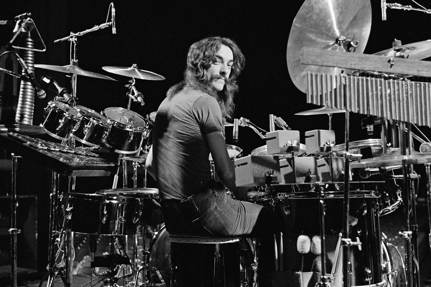 Drummer of the band Rush, Neil Peart, posing with his drumset and other musical instruments